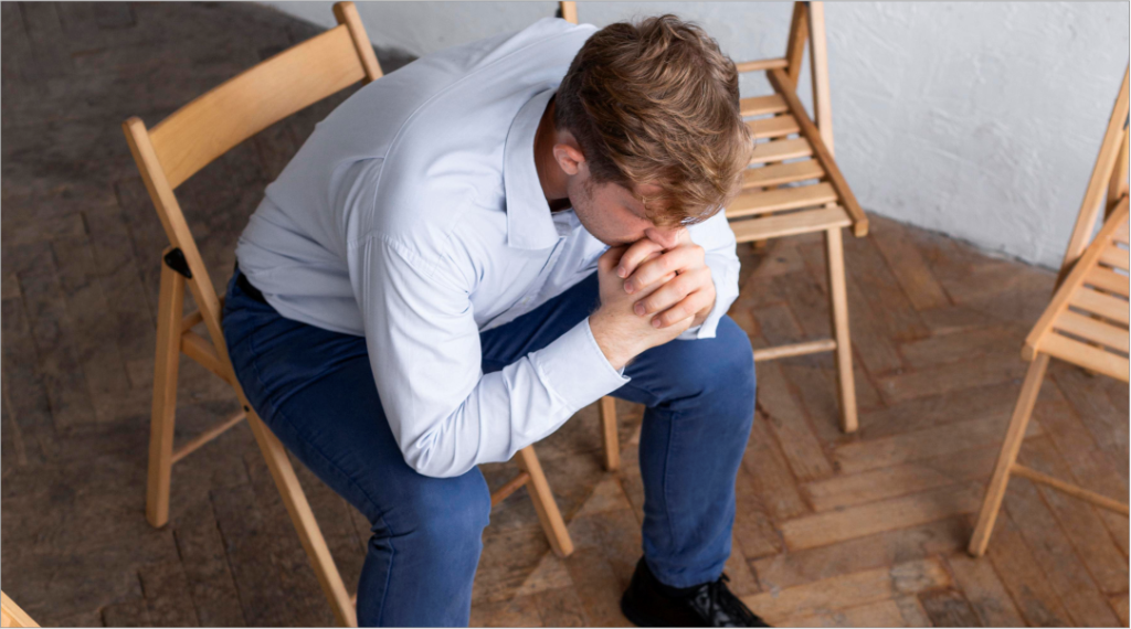 Homem sentado, curvado e em sofrimento, cercado por cadeiras vazias, transmitindo sensação de esgotamento, solidão e limite emocional. A composição deve reforçar a ideia de colapso, mas também de possibilidade de recomeço a partir desse ponto.